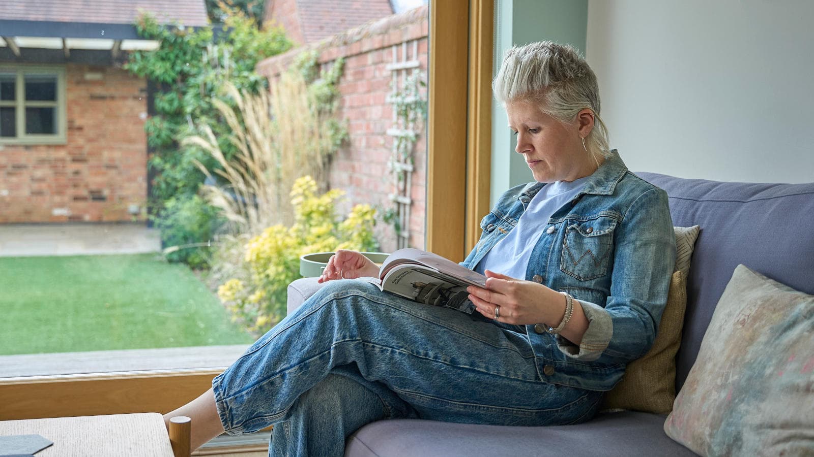 Caroline reading on a sofa beside a window looking onto the garden.